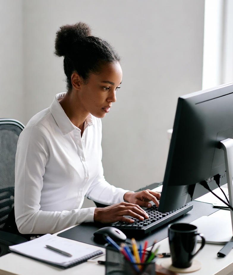 Young Black woman in a white collared shirt typing intently on a computer keyboard at a clean office desk.
